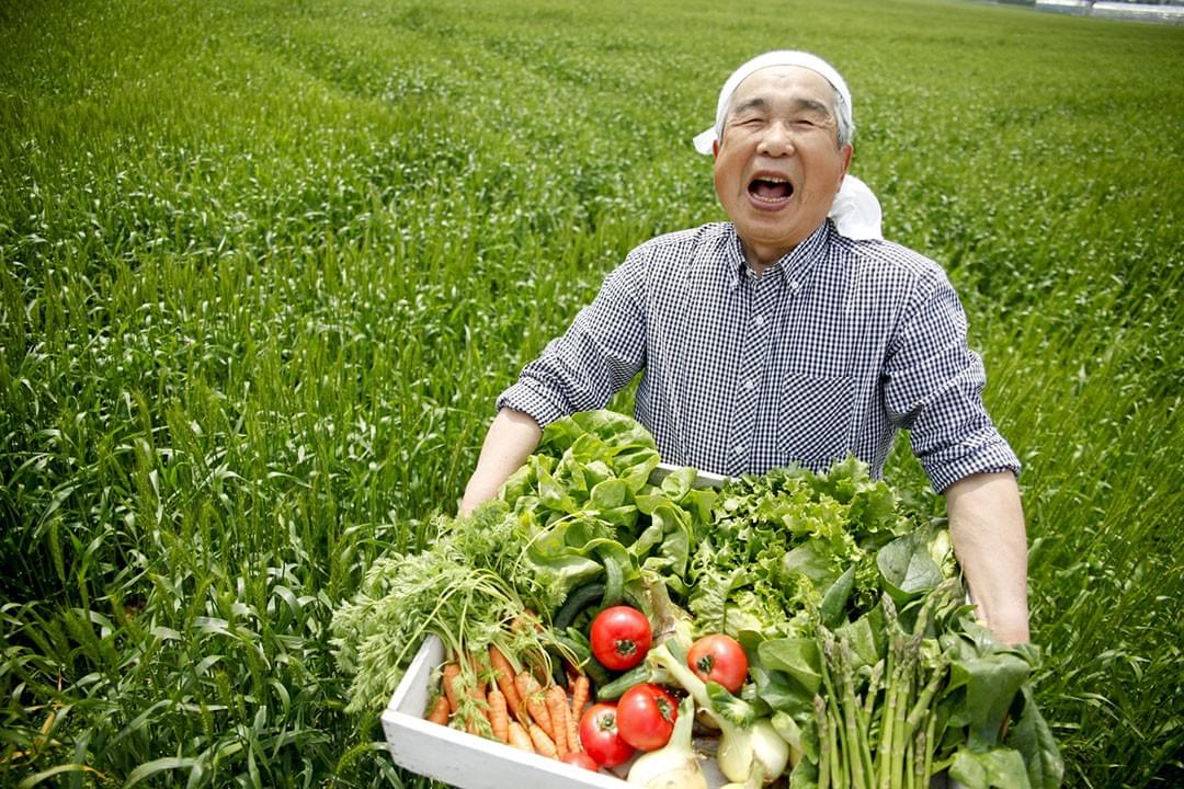 畑で収穫した野菜を手に、笑顔を見せる男性